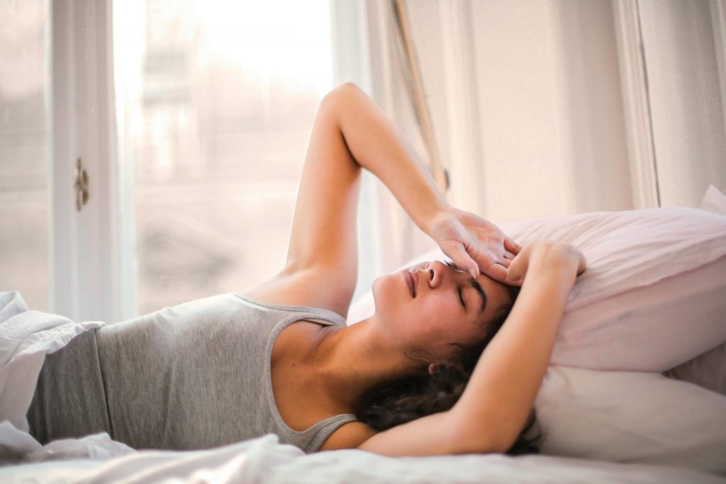 Woman lying in bed looking tired after a full night's sleep, representing sleep exhaustion and fatigue.