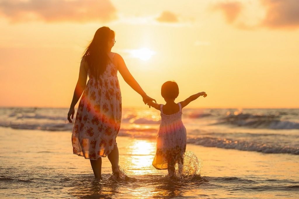 A mother and daughter walking on a beach at sunset, representing the emotional bond central to childhood mental health and early development