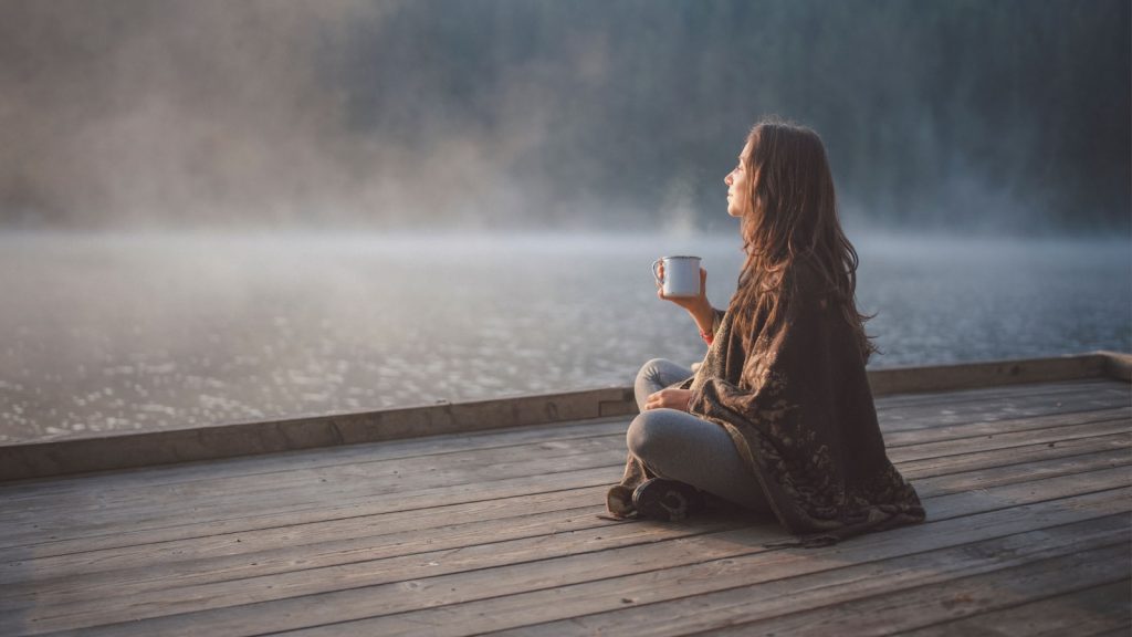 A woman sitting peacefully on a dock with a coffee — a calming morning routine for mental clarity
